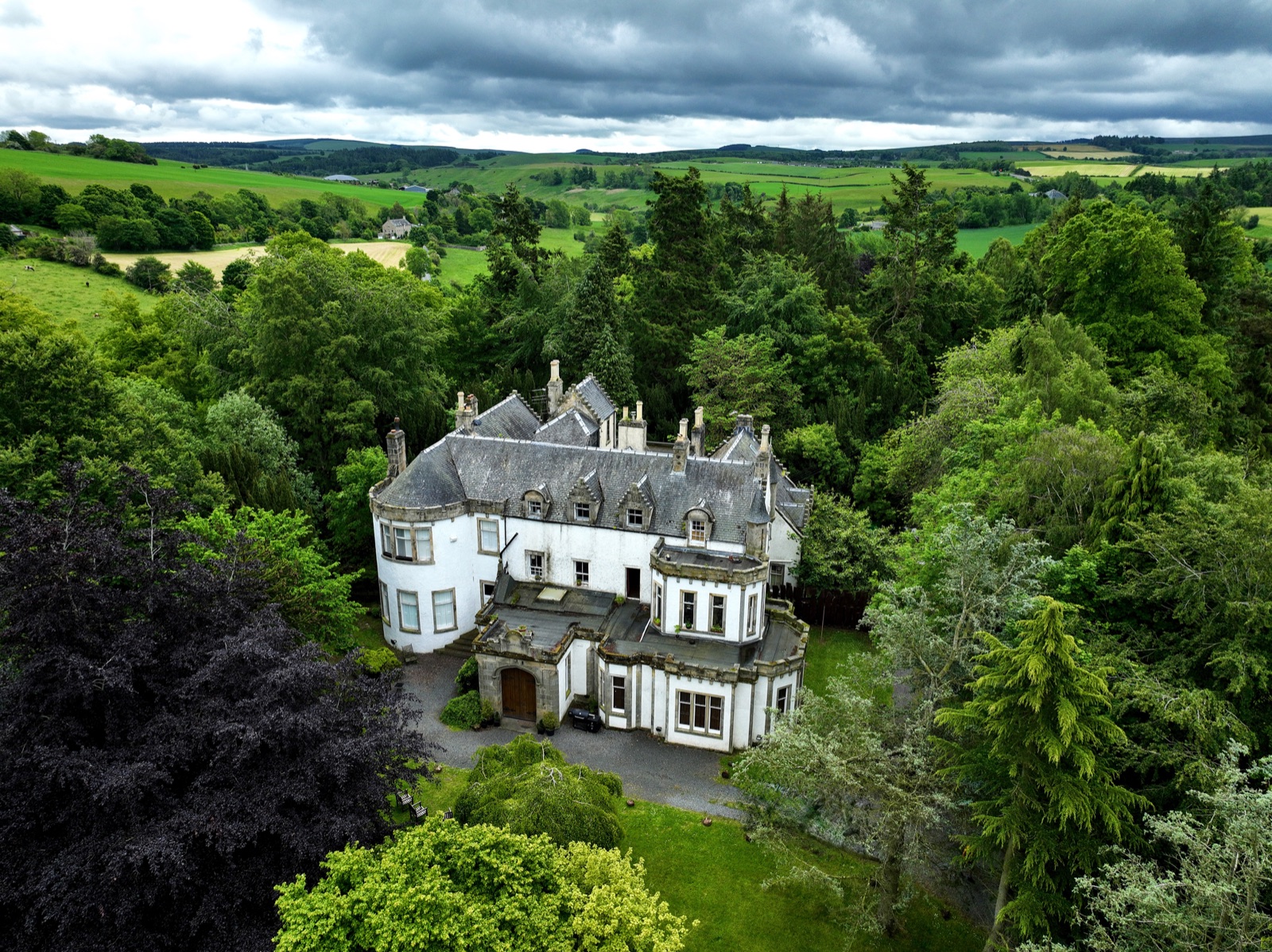 Harvieston Hall seen from above among mature trees.